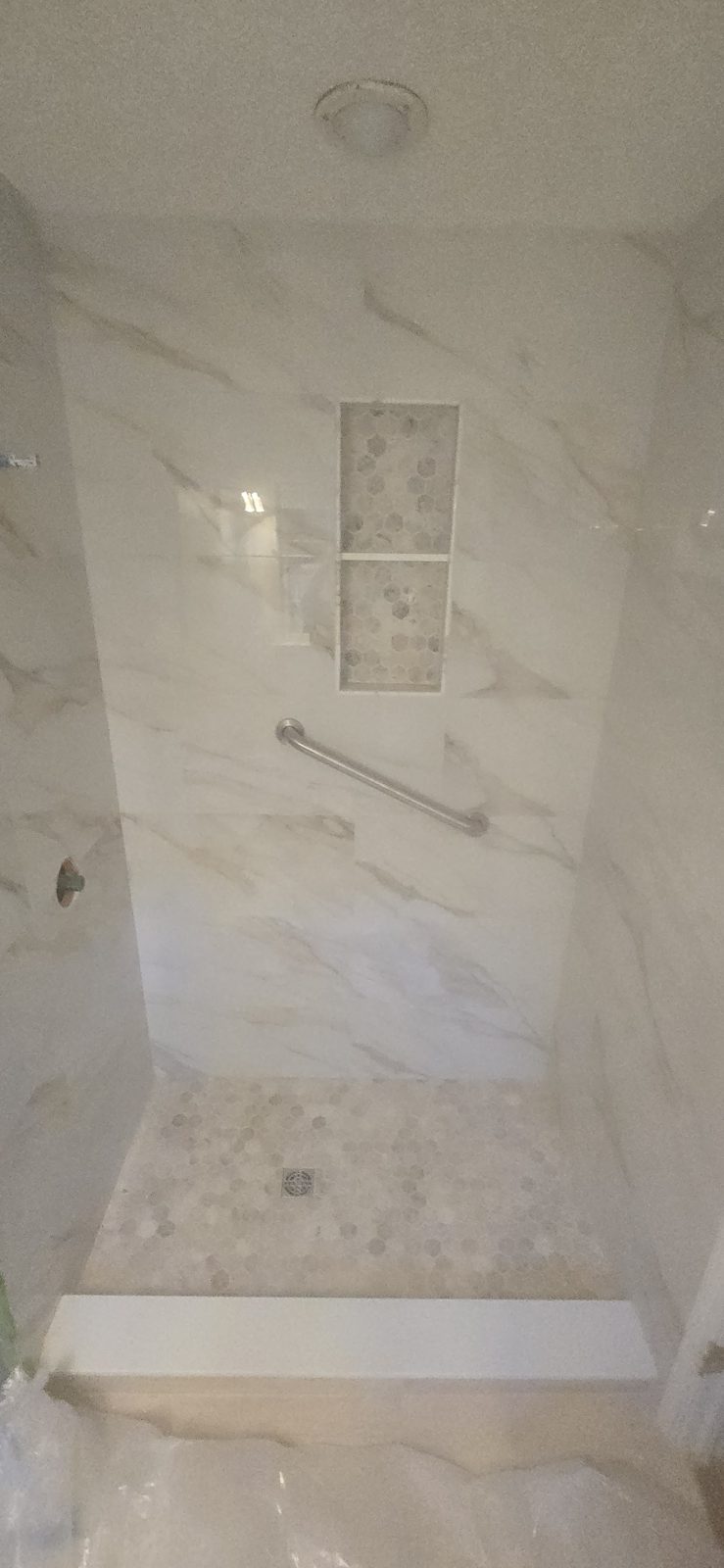 Custom marble-look tile shower with hexagon mosaic niche